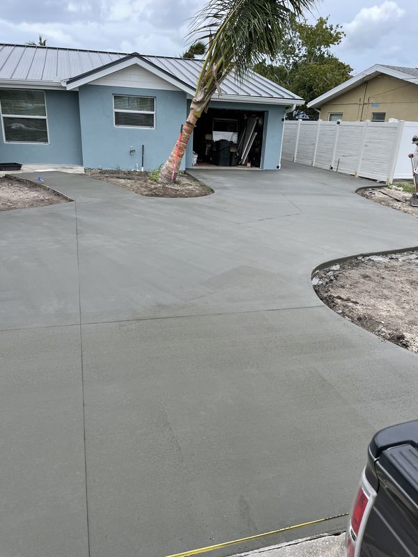 Wide finished driveway wrapping around a palm at a blue coastal home